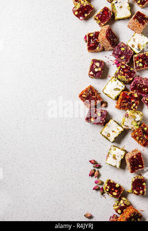 Variety of traditional turkish dessert Turkish Delight different taste and colors with rose petals and pistachio nuts over grey spotted background. Fl Stock Photo