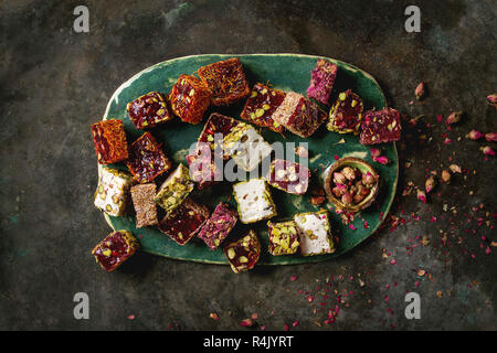 Variety of traditional turkish dessert Turkish Delight different taste and colors with rose petals and pistachio nuts on turquoise ceramic tray over o Stock Photo
