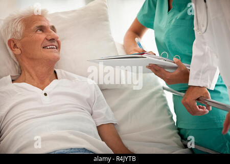 Elderly man in hospital bed,  with a doctor and nurse beside him. Stock Photo