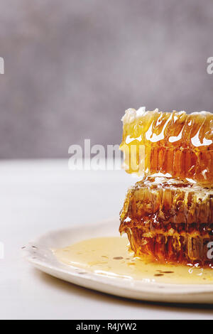 Stack of organic honey in honeycombs in spotted ceramic plate on white marble table. Stock Photo