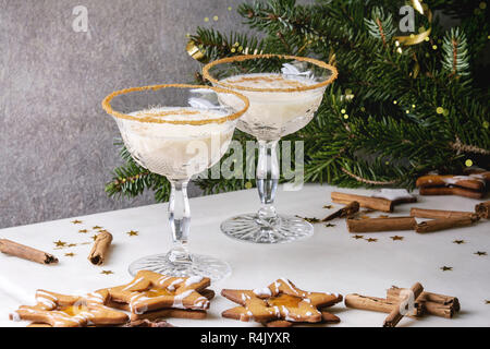 Eggnog Christmas milk cocktail, served in two vintage crystal glasses with shortbread star shape sugar cookies, cinnamon sticks, fir branch over white Stock Photo