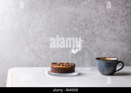 Sweet chocolate tartlet with cup of coffee espresso standing on white marble table with grey wall at background. Minimalist style. Copy space Stock Photo