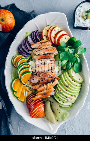 Chicken salad with apples, lettuce, purslane, orange slices in a white salad bowl on a grey background photographed from top view. Stock Photo
