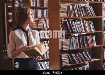 Young attractive student librarian reading a book between library bookshelves Stock Photo