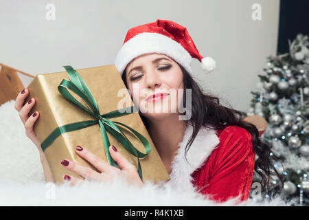 Smiling teenage girl in santa helper hat with many gift boxes on white background. Positive emotional Santa girl. Concept of selling and Christmas shopping. Xmas. Girl hugging gifts. Stock Photo