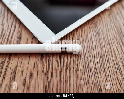 Apple pencil and its cap over a iPad of color white over a wooden surface Stock Photo