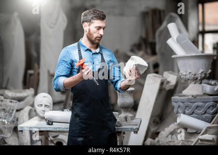 Portrait of a handsome sculptor in blue t-shirt and apron holding a piece of stone in the studio Stock Photo