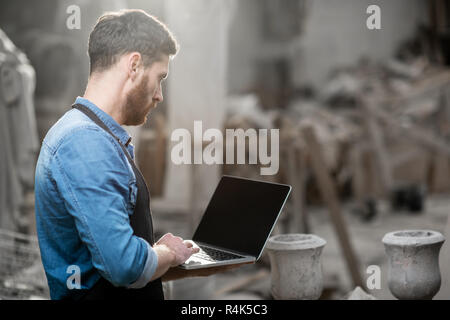 Handsome sculptor working with laptop in the atmospheric studio with old sculptures on the background. Empty screen to copy paste Stock Photo