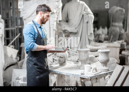 Handsome sculptor working with laptop in the atmospheric studio with old sculptures on the background Stock Photo