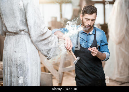 Handsome sculptor smoking a cigarette while resting after the work with sculptures in the studio Stock Photo