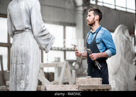Handsome sculptor standing with working tools near the sculpture in the studio Stock Photo