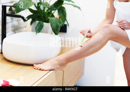 Young woman shaving legs in bathroom Stock Photo