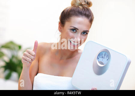 Happy woman holding bathroom scales in bathroom Stock Photo