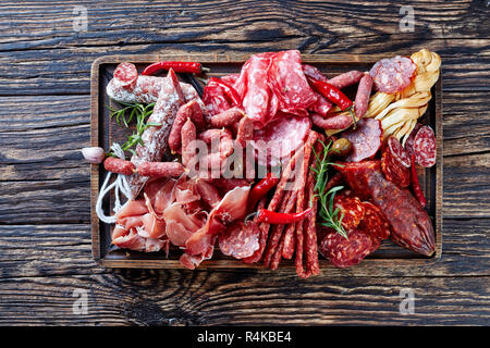 set of meat appetizer - jamon, chistorra, chorizo, salchichon, fuet, olives, tomatoes, chili peppers on a platter on a wooden cutting board on an old  Stock Photo