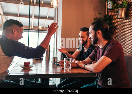 Group of mixed race young men talking in lounge bar. Multiracial friends having fun in cafe drinking coffee Stock Photo
