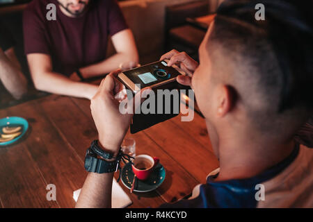 Young arabian man takes a picture of his coffee on his phone for social network. Internet addiction concept. Friends having coffee in bar. Stock Photo