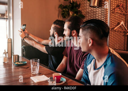 Group of arab friends taking selfie in lounge bar. Mixed race young men having fun in restaurant. Best friends hangout together Stock Photo