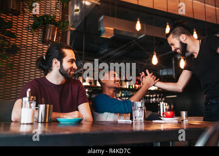Multiracial young men meeting their friend in lounge bar. Real emotions of best friends happy to see each other. Guys shake hands. Friendship Stock Photo