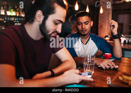 Social network addiction. Two mixed race friends using smartphones in restaurant instead of communicating. Loneliness among friends Stock Photo