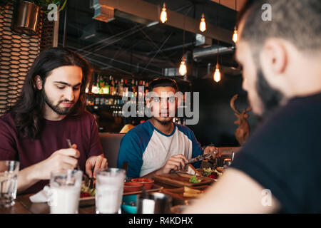 Young arabian men having breakfast in cafe. Best multiracial friends chilling out in bar Hipster guys hangout together Stock Photo
