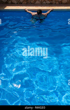 Young, tanned man swimming lengths in a pool with sun reflecting in rippled water and off the tiled floor. Stock Photo