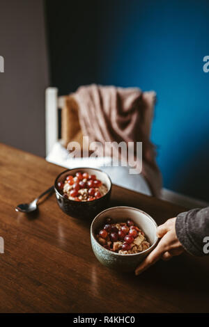 two bowls of porridge with grapes on a wooden table with chair and blanket in the background Stock Photo