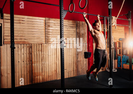 Athletic young man doing pull ups exercises without t-shirt in a crossfit gym Stock Photo