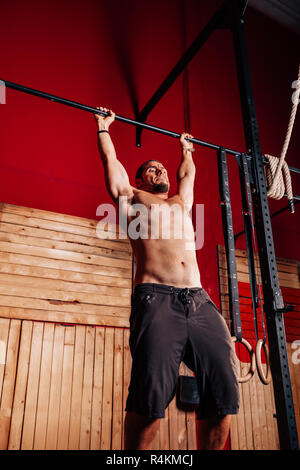 Athletic young man doing pull ups exercises without t-shirt in a crossfit gym Stock Photo