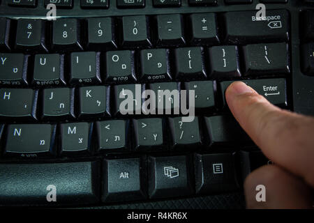 Man typing on a keyboard with letters in Hebrew and English Stock Photo
