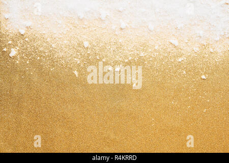 White powdery snow on golden glitter background. Snow and glitter for winter and Christmas gift concept design. Abstract white and gold background. Stock Photo
