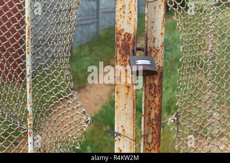 old vintage lock is on the rusty iron gate with ragged rope net in countryside Stock Photo