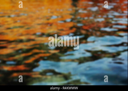 blurred autumn water background with orange and red leaves reflection. waves at lake surface Stock Photo