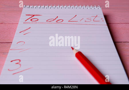 Spiral notebook with  a to-do list written with a red pencil on it, on a pink wooden table Stock Photo