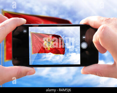 The concept of tourism and travel. The hands of men make a photo from the phone .Shooting from the smartphone flag of Montenegro on the flagpole again Stock Photo