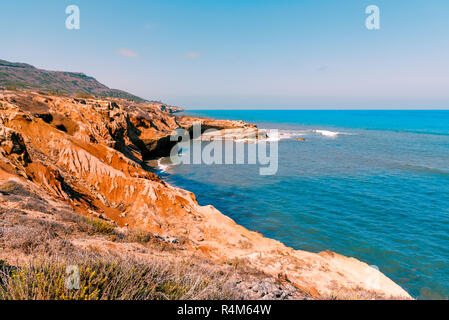 Golden rocky shore line and cliffs with bright blue ocean under a blue sky. Stock Photo
