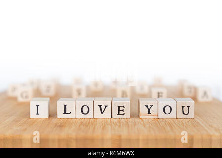 Focus on phrase 'I Love You' made of wooden block dice with letters on a wooden table, random dice mixed up in the background. Shallow depth of field. Stock Photo