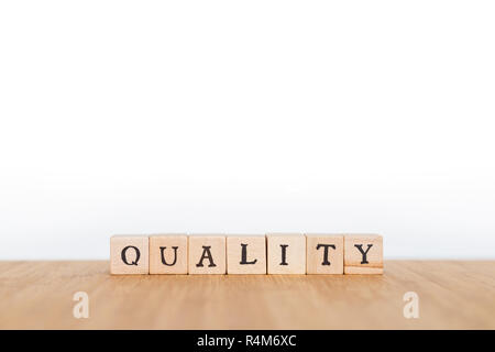 Focus on the word 'Quality' made of wooden block dice with letters on a wooden table. Shallow depth of field. Copy space. Stock Photo