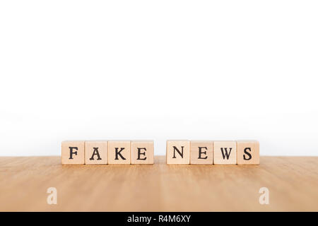 Focus on the phrase 'Fake News' made of wooden block dice with letters on a wooden table. Shallow depth of field. Copy space. Stock Photo