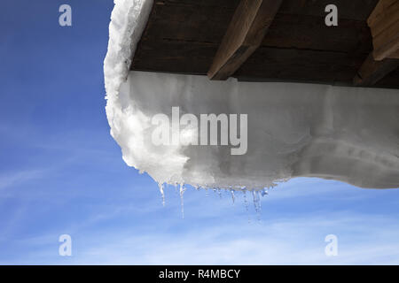 Wooden roof with snow cornice and icicle at sun winter day Stock Photo