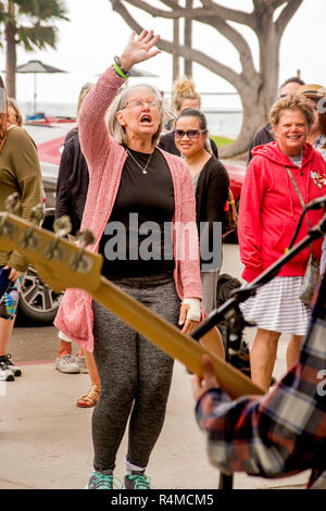 An enthusiastic senior woman waves and sings along with a rock and roll band playing on the street in Laguna Beach, CA, at a citywide music festival. Stock Photo
