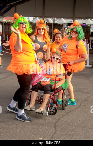A wheelchair-bound senior woman is joined by her adult daughters in funny costumes as they all prepare to run in a county fair community foot race in Costa Mesa, CA. Stock Photo