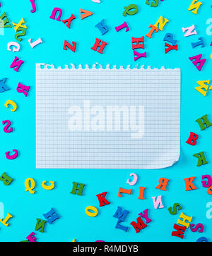 white sheet torn from a notebook on a blue background with multicolored letters of the English alphabet Stock Photo