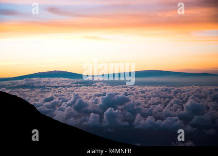 Beautiful Colorful Sunrise Sky at Dawn from the Top of Haleakala Volcano in Maui Hawaii Above the Clouds with Mountains in Background of Landscape Stock Photo
