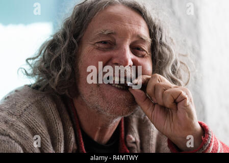 Senior homeless man with a few of his teeth missing smiling as he bites in to a piece of dark chocolate. Stock Photo