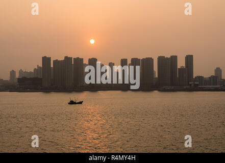 Sun rising behind the tall city skyline of Qingdao in China Stock Photo