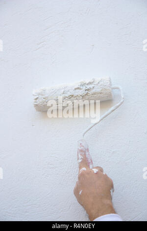 A wall is being painted by the professional painter using a roller with white paint Stock Photo
