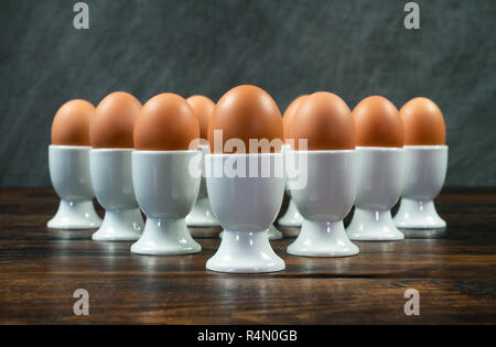 Ten boiled eggs in white egg cups on a wooden table in a triangle arrangement Stock Photo