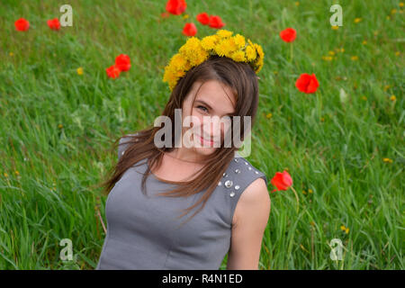 A girl with a wreath of dandelions on her head. Beautiful fairy young girl in a field among the flowers of tulips. Stock Photo