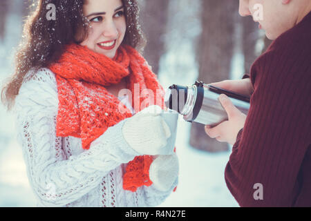 Young couple pours hot tea out of thermos in winter forest Stock Photo