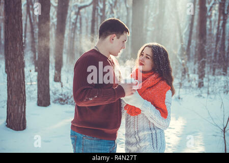 Young couple drinks tea in winter forest. Young people having picnic outdoors together Stock Photo
